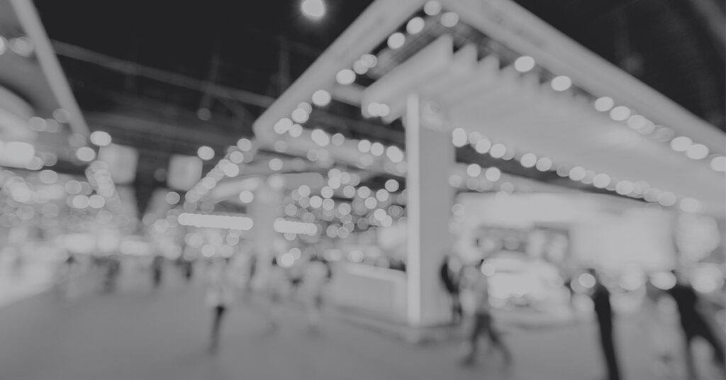 mistakes that you are making at a trade show as an exhibitor. A blurry show floor is pictured with trade show exhibits and visitors walking the show aisles