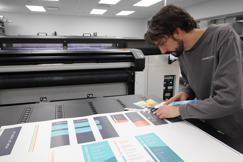 print technician in calgary comparing test prints to Pantone colour swatches on a large format printer