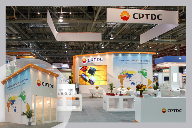 50x50 custom island trade show booth for the Global Petroleum show in Calgary, Alberta, Canada. Two "L"-shaped fabric signs with the company name are suspended above the display from the ceiling. A double-decker video wall is features with 16 monitors put together. And adjacent wall features a large map graphic of the company's locations around the word. The bottom left insert in the photograph shows the other side of the wall, which is a private enclosed meeting space with frosted glass windows and doors. There is a 3D logo mounted above, and the ceiling overhang features custom potlights. The rest of the booth space features comfortable white bucket chairs and tables, and custom counters that showcase equipment. 