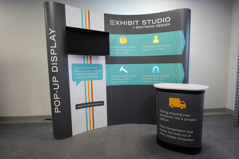 10ft portable pop-up trade show display in Calgary, Alberta. This display features a built-in monitor, graphic magnetic panel and decals, along with backlit logo cutouts and a portable podium. 