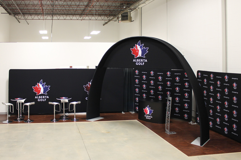30ft portable event display with fabric backdrop walls, a curved overhead arch, rental seating and flooring, and a customized reception counter. 