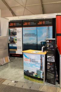 10x10 trade show booth in Calgary with 3 banner stands against the back wall, a portable branded podium, and portable mesh literature rack