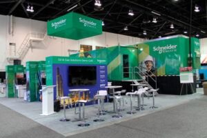 large custom trade show exhibit for the Global Energy Show in Calgary, Alberta. A rigged fabric sign is seen from all sides as it suspends from the ceiling. Multiple wall and monitor panels demo products. A variety of seating areas and counters to meet with clients are included. To the right is a large worksite trailer that has been covered is custom wall graphics by our team.