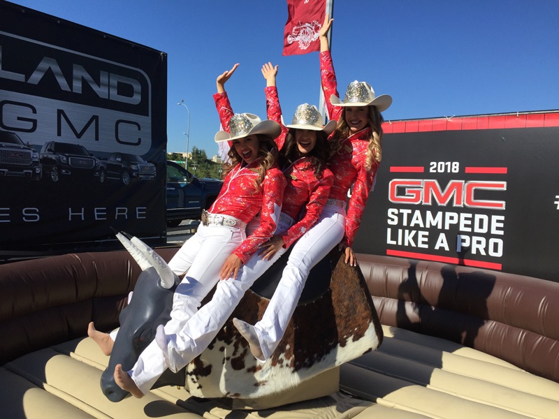 inflatable mechanical bull rental in Calgary during the Calgary stampede. Three cowgirls pose while sitting on the bull in front of a branded outdoor backdrop for GMC.