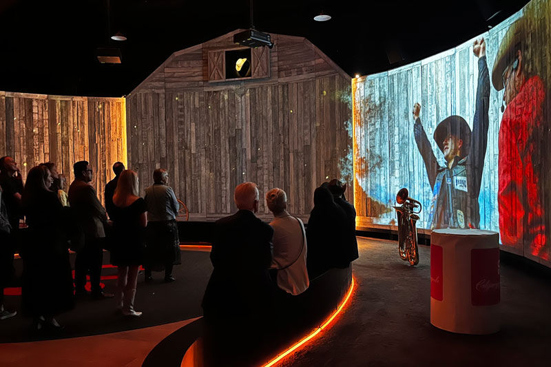 horseshoe-shaped barnwood wall that serves as the backdrop for a multimedia video show. Benches line the perimeter with amber-glowing LED light strips.
