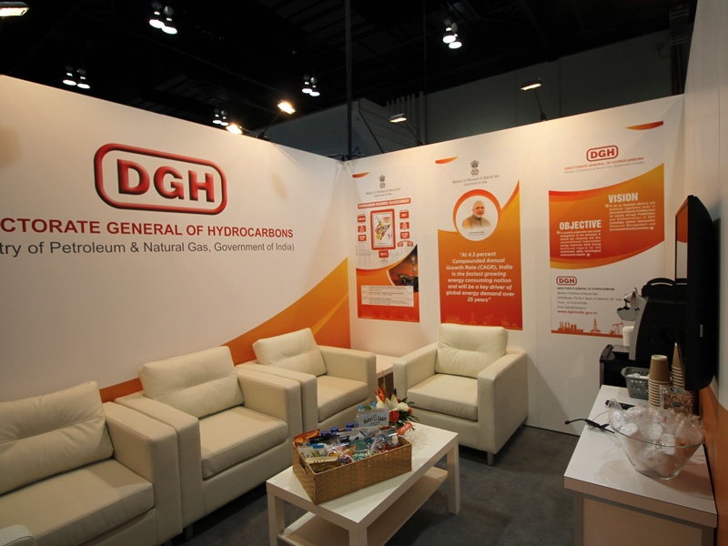 private meeting area within a trade show booth that includes walls with branded graphics, comfortable armchairs and coffee tables, along with rental counters. 