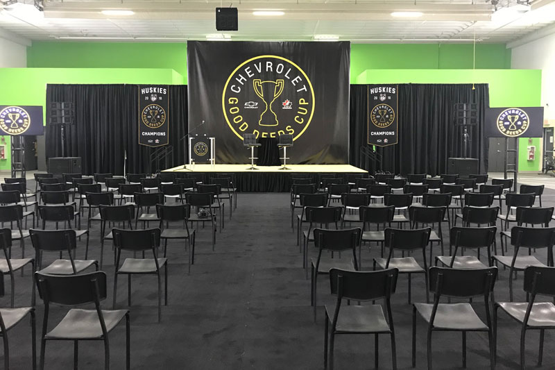 branded event stage in Manitoba with rental black carpet and rows of black chairs facing the front of the stage.