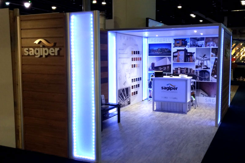 custom backlit 10x20 trade show booth display in Vancouver. The corner panels of the walls and ceilings have LED strip lighting. Half the booth is covered by a canopy, where the interior walls host products and a branded counter. 