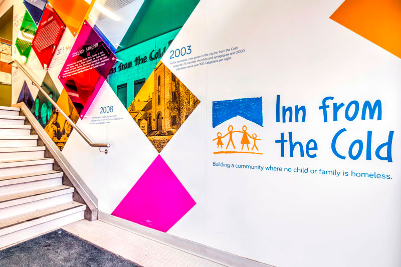 dynamic donor recognition wall for Inn from the Cold in Calgary. Vinyl wall graphics and text are implemented showing the history of the organization, as well as colourful dimensional panels recognizing donors and their monetary contributions.