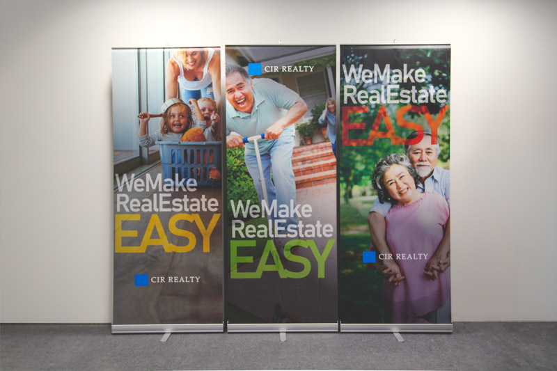 set of 3 retractable banner tands for a real estate company in Calgary, Alberta. The text reads "We make real estate easy" with imagery of families having fun indoors and outdoors. 