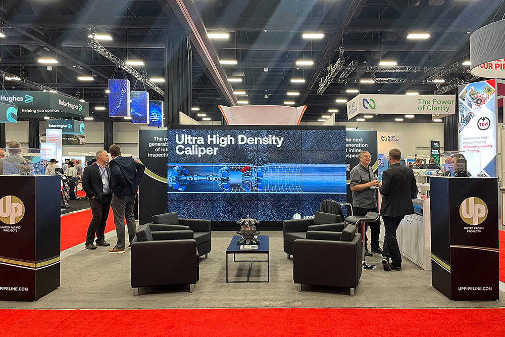 20x20 peninsula trade show booth at a trade show event in Calgary. The back is a video wall with a seating area placed in the centre. Two graphic pillars are at the front of the booth on the corners, and a counter on the right perimeter of the booth. 