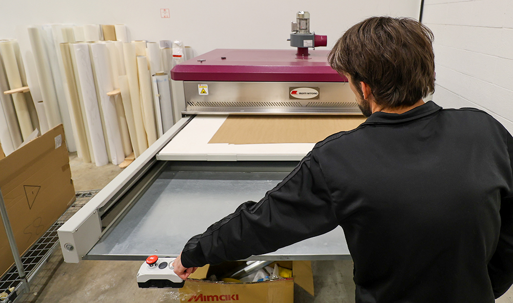 Print and graphic technician in Calgary Alberta standing in front of a dye sublimation heat press. The flatbed printer area uses heat and pressure to create a permanent colour bond on the substrate. 