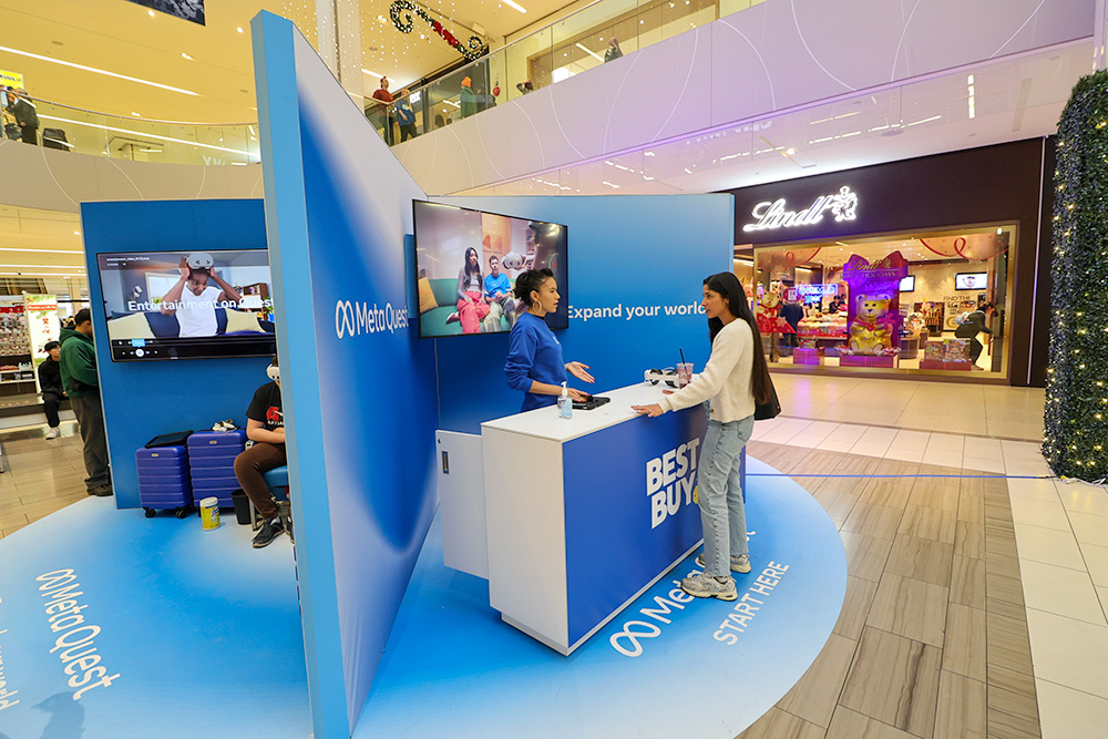 cross-section of an open-concept retail pop-up display showing two women interacting in front of a branded Best Buy counter. 