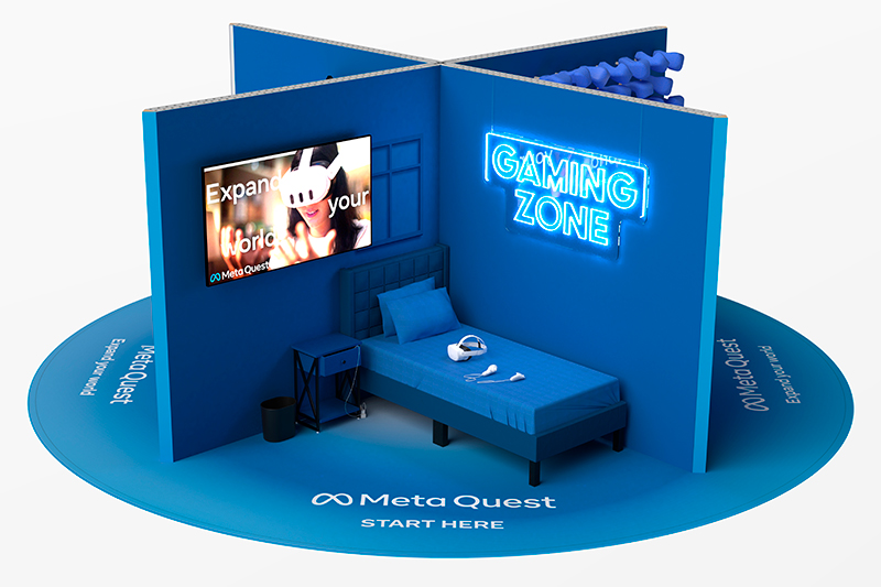 10x10 open-concept marketing display for a VR headset from Meta. There are 4 room areas that form the shape of an "X" from a birds eye view above. The corner shown features a twin bed, wall-mounted monitor and  LED "Gamzing Zone" sign for users to test out the product. 